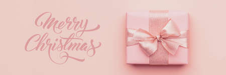Christmas banner. Beautiful pink christmas gift isolated on pastel pink paper background.の写真素材