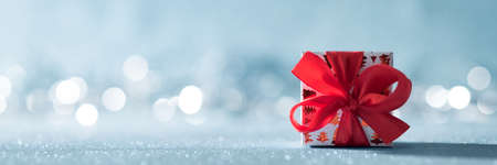 Beautiful red christmas gift with large bow on shiny blue background and defocused christmas lights in the background. Christmas banner with copy space.の写真素材