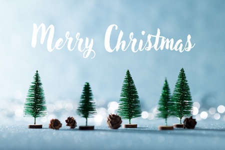 Magical winter wonderland background. Miniature evergreen trees and pine cones on shiny blue...
