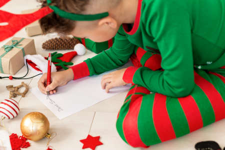 Cute boy wearing christmas pajamas writing letter to Santa on livingroom floor. Overhead view of a young boy writing his christmas wishlist.の写真素材