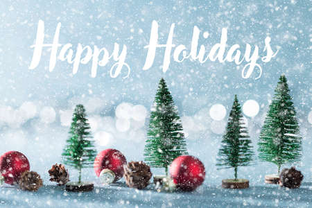 Magical snowy miniature winter wonderland background. Evergreen trees, pine cones and red christmas baubles on shiny blue background with bokeh in the background.の写真素材