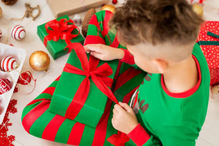 Curious young boy wearing xmas pajamas sitting on the floor, opening his christmas present, top view.の写真素材