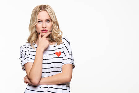 Attractive young confident woman wearing casual clothes thinking, with hand on chin, looking at camera and standing isolated over white background.の写真素材
