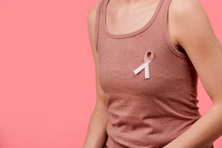 Midsection of a young woman wearing pink breast cancer awareness ribbon isolated over living coral background. Healthcare, people, charity and medicine concept.の写真素材