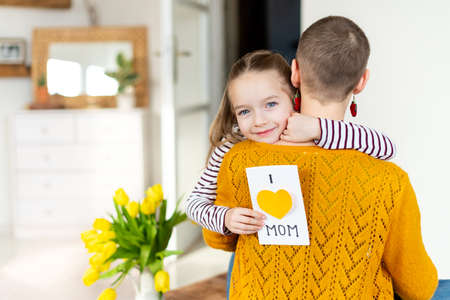 Happy Mother's Day or Birthday Background. Adorable young girl giving her mom, young cancer patient, homemade I LOVE MOM greeting card. Family celebration concept.の写真素材