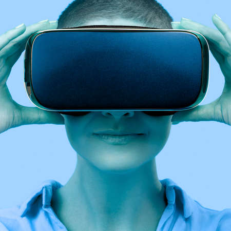 Young woman wearing virtual reality goggles. Woman wearing VR glasses over blue background. VR...