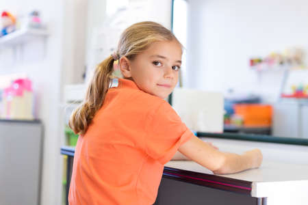 Young girl in speech therapy office. Smiling happy girl sitting in front of a mirror, waiting for speech therapist.の写真素材