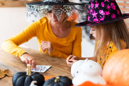 Cute young girl sitting at a table, decorating little white pumpkins with her mother. DIY Halloween holiday and family lifestyle background.の写真素材