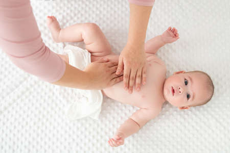 Baby massage. Female therapist gently massaging newborn baby boy. Mother applying body lotion to her...