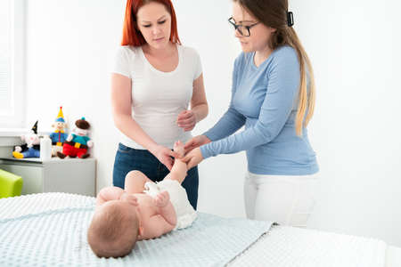 Female massage therapist teaching young mother how to massage her newborn baby boy. Baby massage concept. の写真素材
