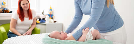 Female massage therapist or a doctor examining newborn baby boy with the mother watching in the background. Baby massage banner.の写真素材