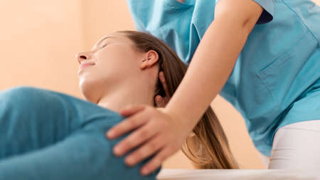 Female physiotherapist or a chiropractor adjusting patients neck. Physiotherapy, rehabilitation concept. Side view cropped shot.の写真素材