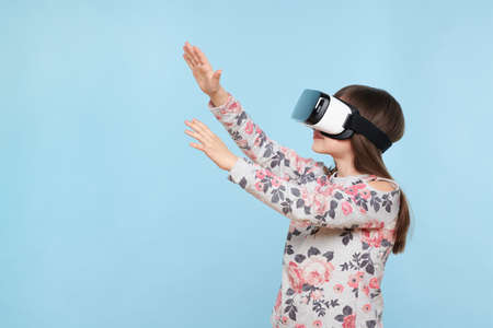 Studio portrait of cute young caucasian girl wearing virtual reality glasses against pastel blue...