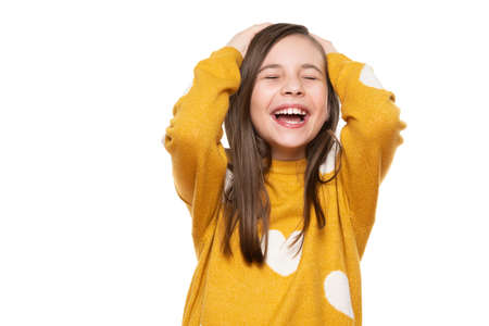 Waist up studio portrait of an adorable young girl laughing with excitement, head in hands and...