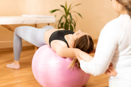 Physiotherapist working with young female client on core strength using fitball. Rehabilitation and physiotherapy background.の写真素材