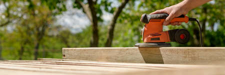 Unrecognizable man in the garden sanding wooden planks. DIY home improvement, restoration, carpentry concept. Hand detail banner with copy space.の写真素材