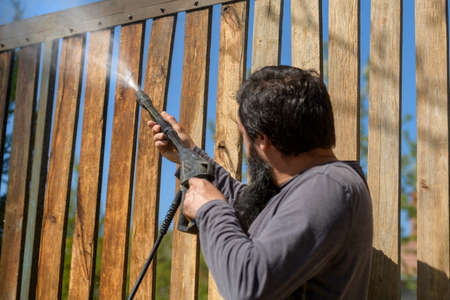 Unrecognizable man cleaning a wooden gate with a power washer. High water pressure cleaner  used to DIY repair garden gate.の写真素材