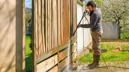 Mid adult man cleaning a wooden gate with a power washer. High pressure water cleaner used to DIY...