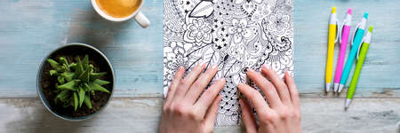 Adult coloring book, stress relieving trend. Art therapy, mental health, creativity and mindfulness concept. Flat lay close up on woman hands coloring an adult coloring book banner.の写真素材