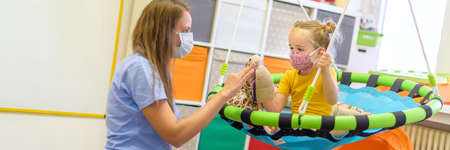 Toddler girl in child occupational therapy session doing playful exercises with her therapist during...