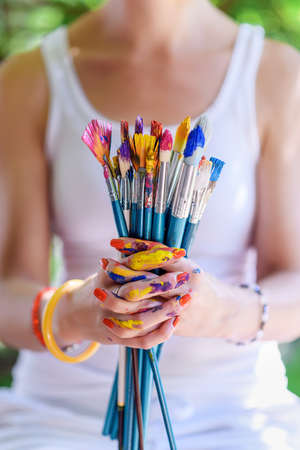 Young female painter artist holding a bunch of dirty used paintbrushes. Funky lifestyle creative hobbies background.の写真素材