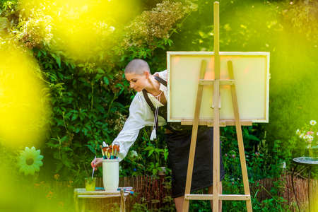 Beautiful young woman relaxing while painting an art canvas outdoors in her garden. Cancer survivor, mindfulness, art therapy, creativity concept.の写真素材