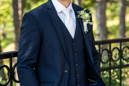 Unrecognizable young groom in elegant dark blue suit with beautiful white roses boutonniere. Groom fashion detail shot.の写真素材