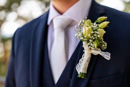 Unrecognizable young groom in elegant dark blue suit with beautiful white roses boutonniere. Groom...