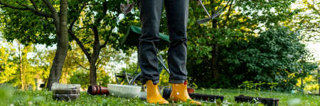 Unrecognizable female gardener standing in her ornamental backyard garden. Planting seedlings,...
