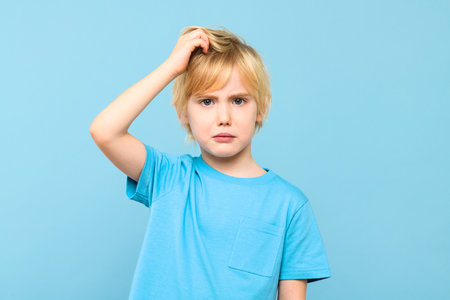Young doubtful confused boy thinking, scratching head, trying to find solution, isolated on pastel blue background.の写真素材