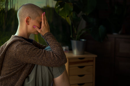 Young female cancer patient with head in hands indoors portrait. Mental health, emotional support, struggles and coping mechanisms during cancer illness.の写真素材