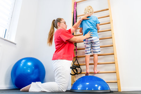Young boy with female physical therapist exercising on wall bars during therapy session. Child occupational physical therapy.の写真素材