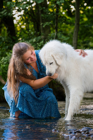 Young woman and her large white Great Pyrenees dog enjoying time together, cooling off in a stream...
