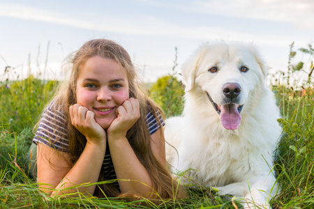 Beautiful young woman and her cute large white Great Pyrenees dog laying in tall grass meadow,...