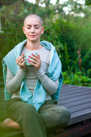 Young female cancer patient sitting on garden patio with coffee, eyes closed. Mental health, wellbeing, life balance, meditation during illness.の写真素材