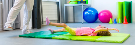 Child with physical disability in physical therapy session. Child living with cerebral palsy exercising with her therapist during physiotherapy.の写真素材
