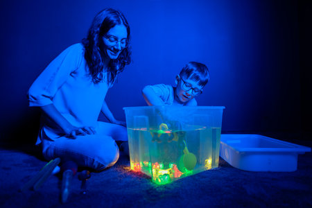 Child and therapist in sensory stimulating room, black snoezelen. Autistic child playing with...