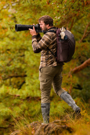 Nature photographer. Young male photographer autumn season outdoors portrait. Back view. Landscape photographer taking photos.の写真素材
