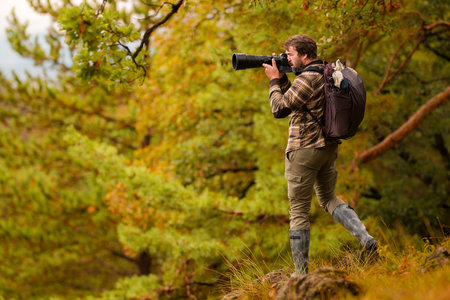 Nature photographer. Young male photographer autumn season outdoors portrait. Back view. Landscape photographer taking photos.の写真素材