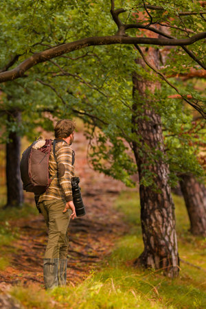 Nature photographer. Young male photographer autumn season outdoors portrait. Back view. Landscape photographer taking photos.の写真素材