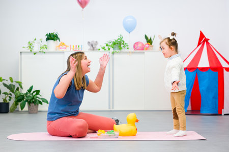 Toddler girl with Down syndrome in child occupational therapy session doing sensory playful exercises with her therapist. Child therapy, neurodiversity, learning difficulty, developmental disability.の写真素材
