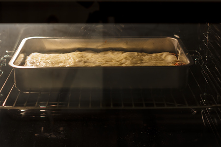Lasagna in a metal container is cooking in ovenの写真素材