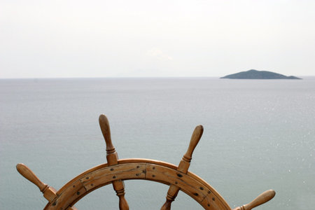 Old ship's steering wheel on great ocean background with a small island ahead.の写真素材
