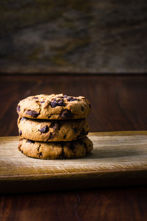 A pile of dramatically illuminated cookies before a dark wooden background