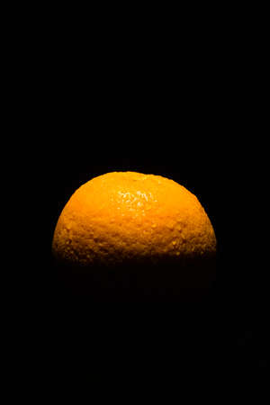 Dark low key image of a fresh and ripe orange fruit lit from above onlyの写真素材