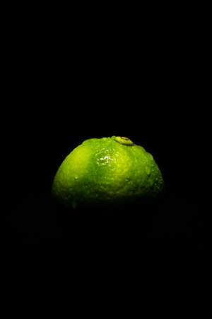 Dark low key image of a fresh and ripe green lime fruit lit from above onlyの写真素材