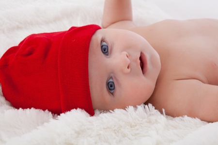 Adorable baby boy lying on soft fur blanket and cushion, smiling with red hat onの写真素材