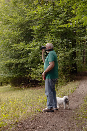 Man with binoculars looking at the dog in the forest.