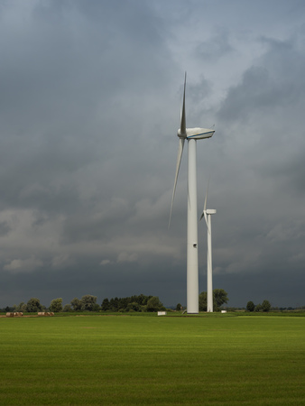 Wind turbines illuminated by sunrays and dramatic sky on a stormy summer dayの写真素材