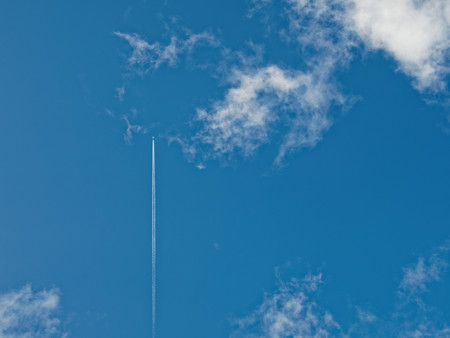airplane flies between bright white clouds and blue sky on a sunny dayの写真素材